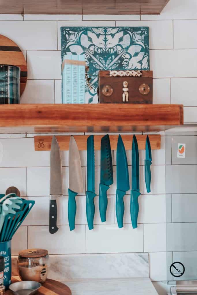 A set of vibrant blue kitchen knives hanging on a wooden strip in a modern kitchen setting.