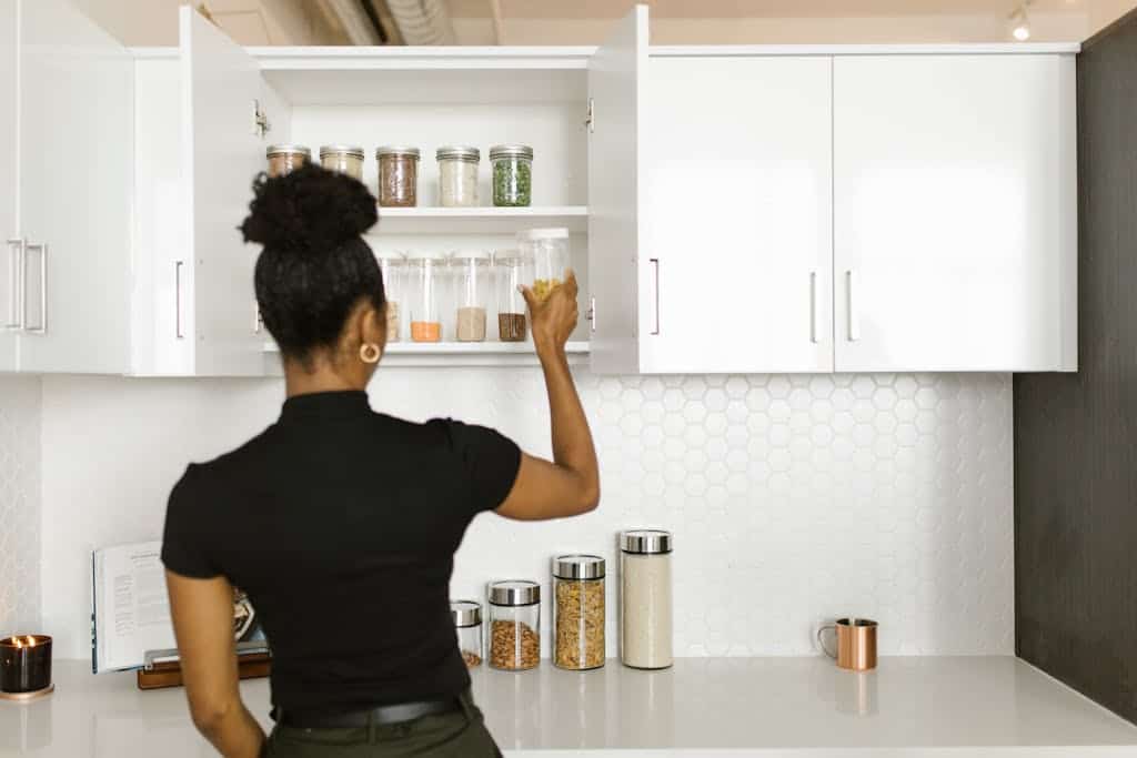 A woman organizing a pantry shelf with various food jars in a modern kitchen.