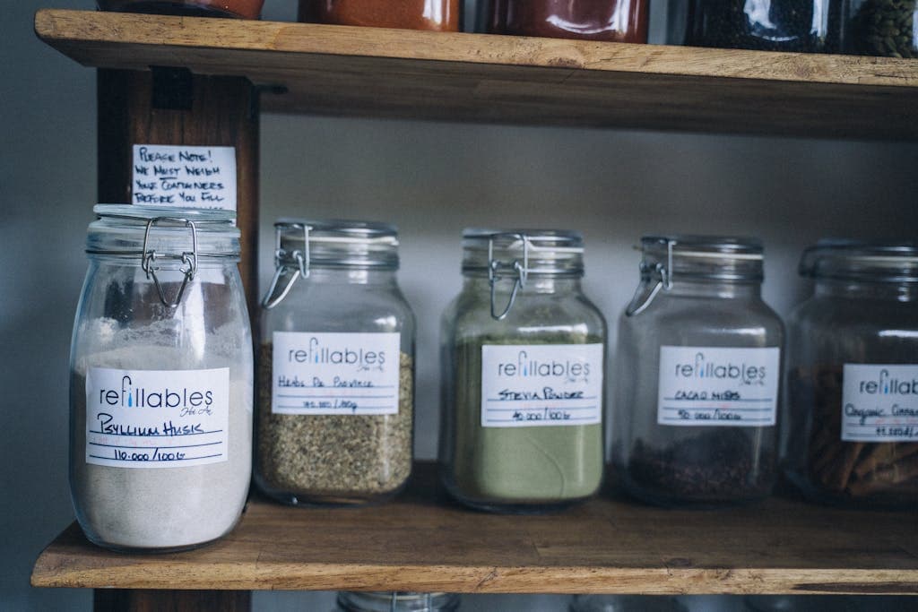 Assorted refillable glass jars with organic goods on a wooden shelf.