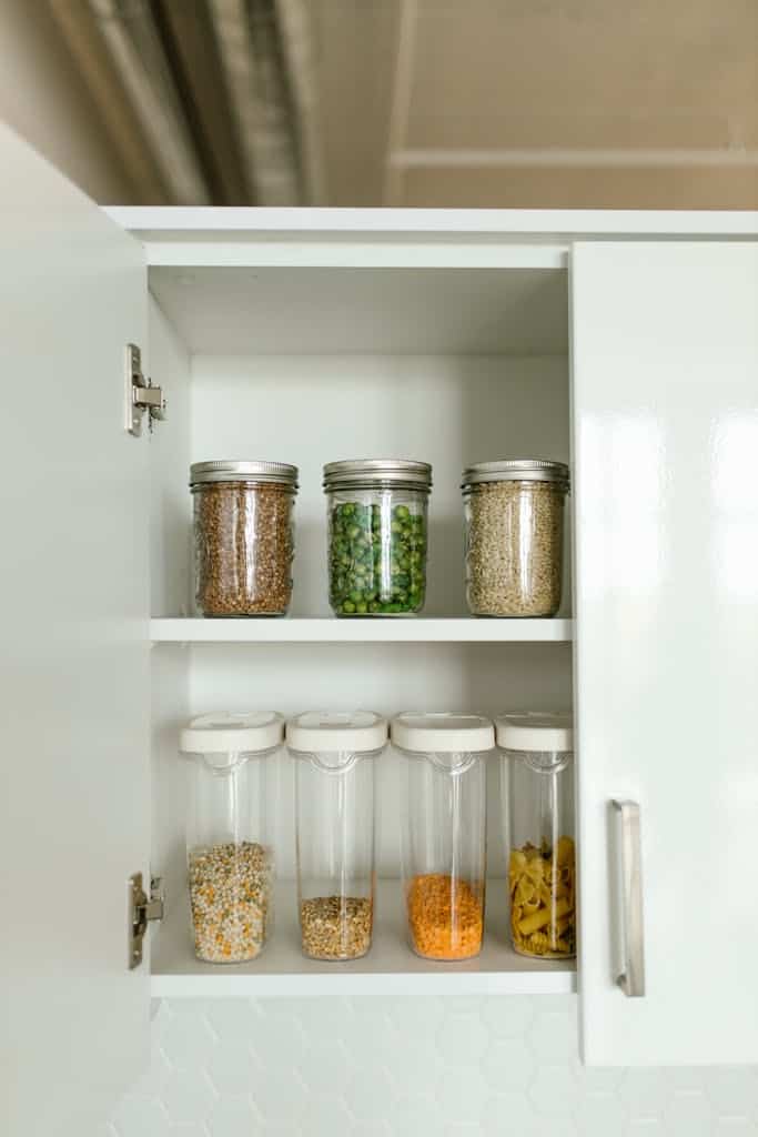 Neatly organized kitchen cabinet with various food items in jars and containers on shelves.