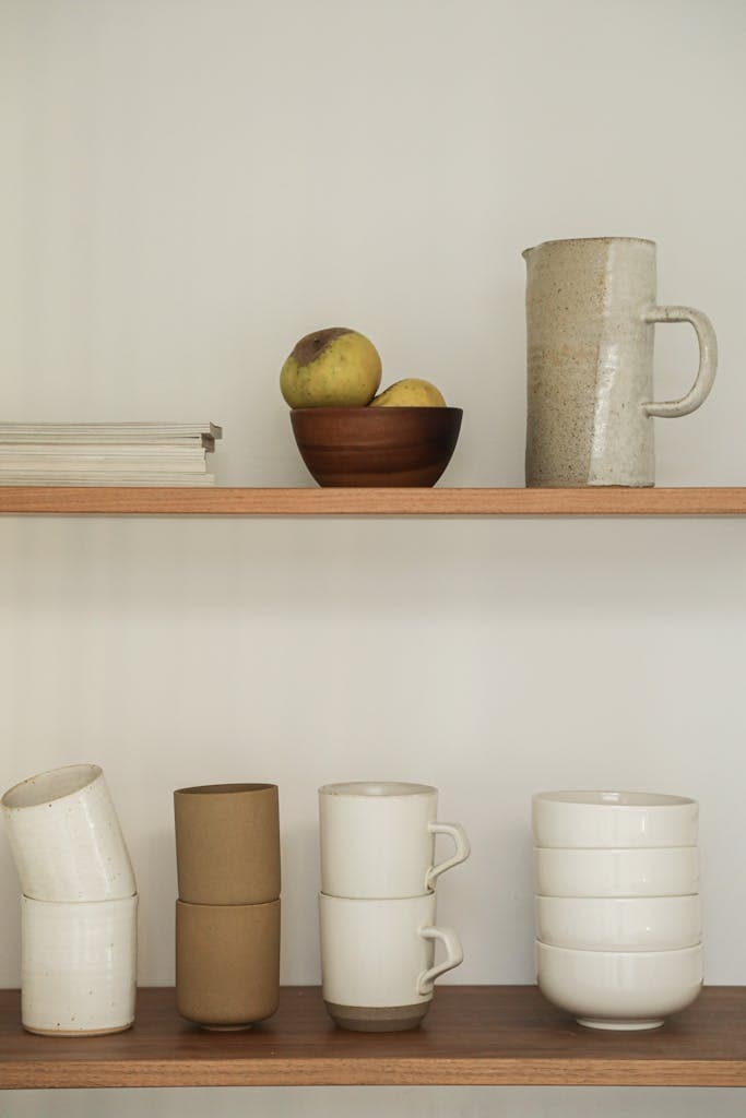 Stylish kitchen shelf with stacked cups and a rustic pitcher, perfect for modern interiors.