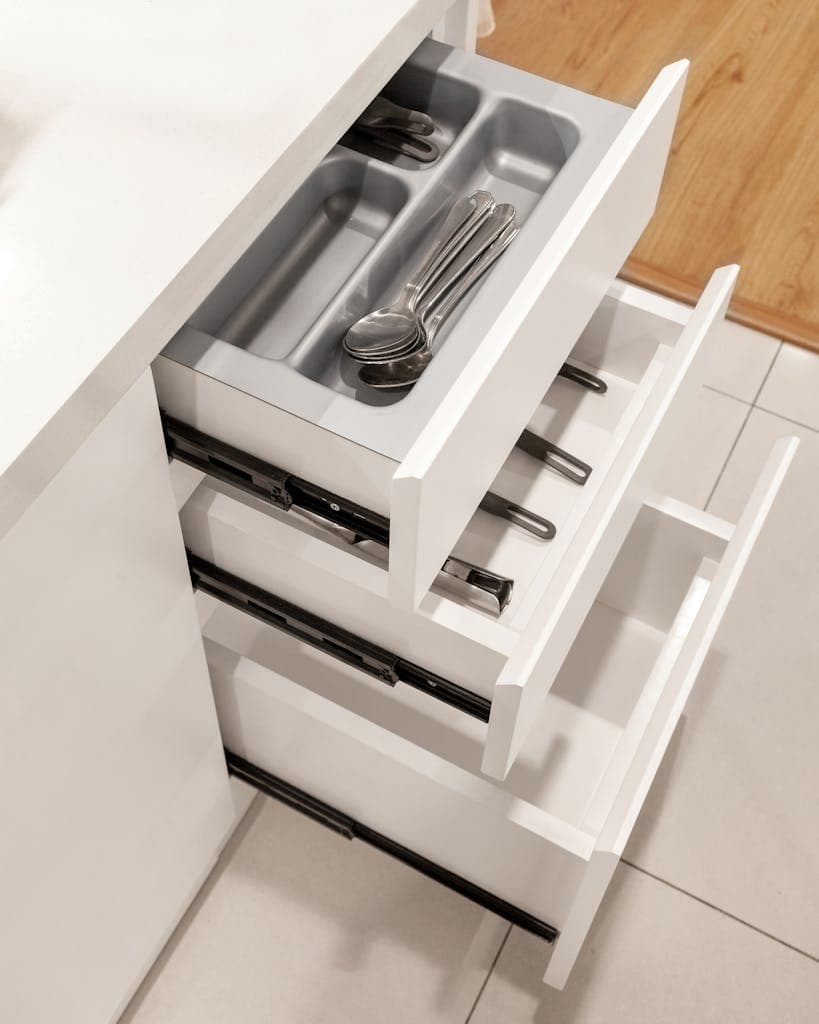 Top-down view of open kitchen drawers featuring a utensil organizer with spoons.