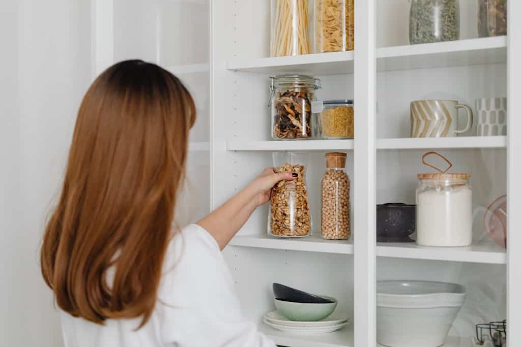 Woman arranging jars on pantry shelves for organized food storage.